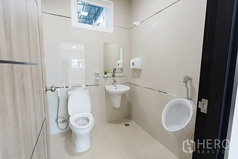 Warehouse for rent in Bang Bo, Samut Prakan - Clean industrial restroom with toilet, urinal and wall-mounted sink inside the warehouse office.