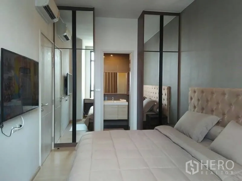 Condominium for rent in Huai Khwang, Bangkok - Master bedroom with mirrored wardrobes, upholstered headboard and doorway to the ensuite bathroom.