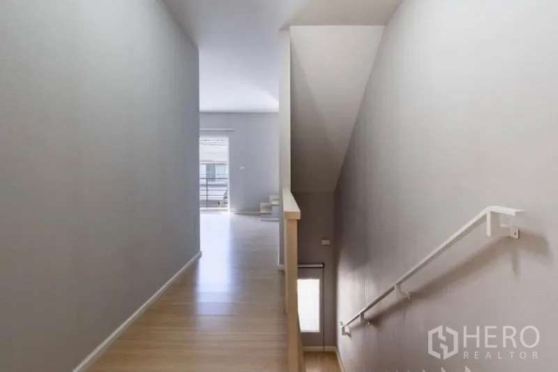 Townhouse for rent or sale in Watthana, Bangkok - Upper-floor corridor and stairwell with natural light and wood floors.