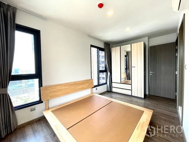 Condominium for rent in Chatuchak, Bangkok - Sunlit bedroom with wooden bed frame, mirrored wardrobe and city outlook.