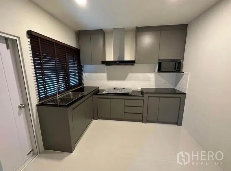 Detached House for rent in Bang Phli, Samut Prakan - Fitted kitchen with grey cabinetry, black countertops, range hood and window blinds.