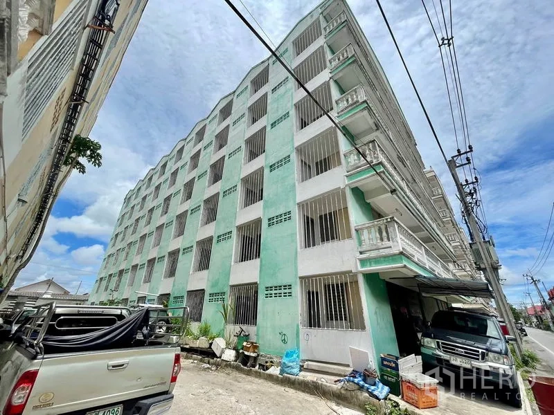 Apartment for sale in Mueang Samut Prakan, Samut Prakan - Street view of green mid-rise apartment exterior with barred windows.