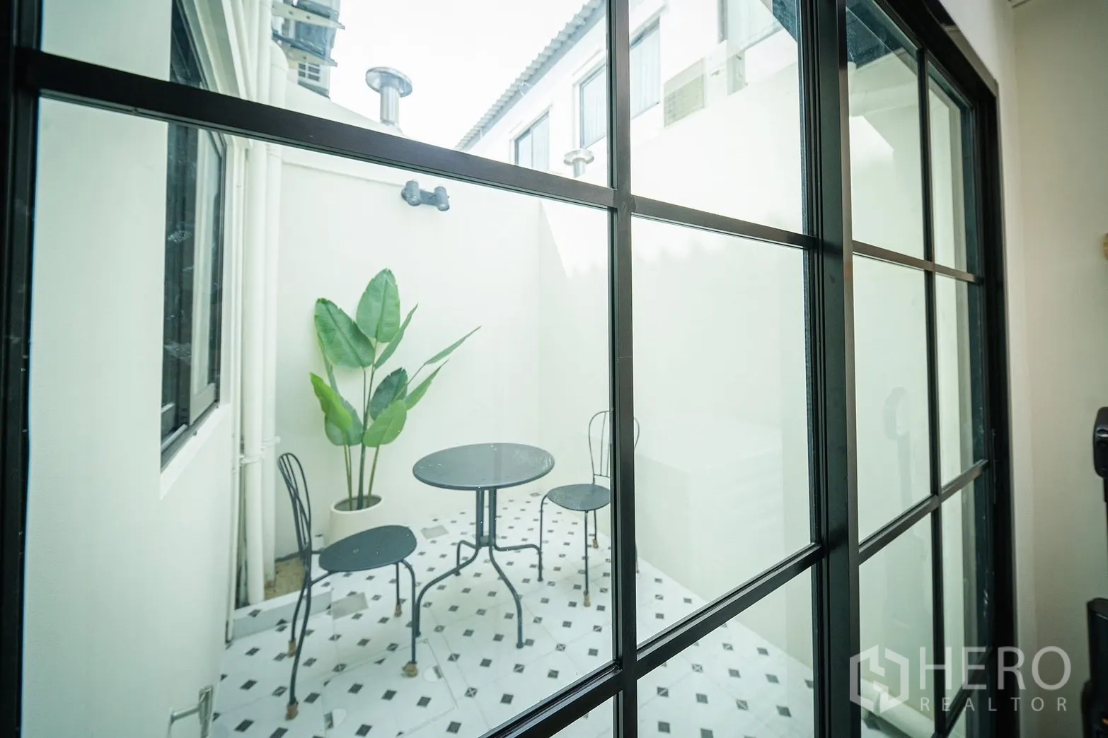 联排别墅 for rent in Bang Phli, Samut Prakan - 透过黑框推拉门可见小型瓷砖庭院，设有圆桌与椅子。