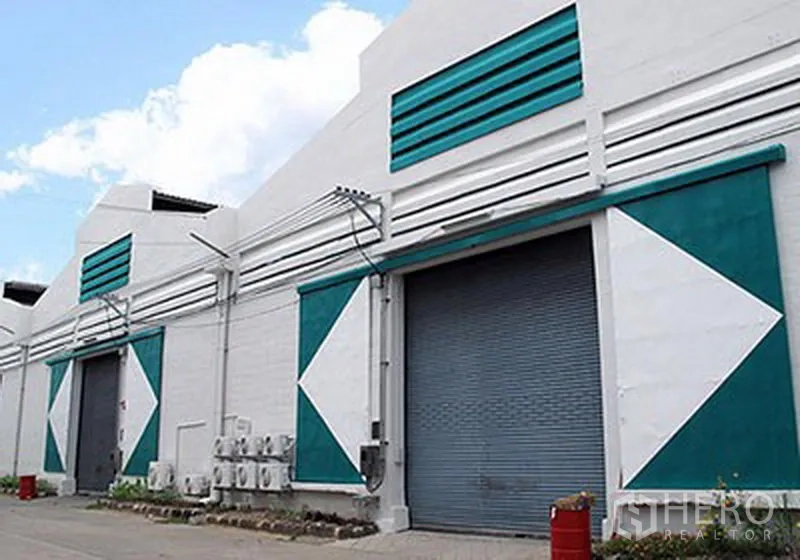 货栈 出租在Prawet, Bangkok - 多间仓库门面一排，青绿与白色装饰，配多扇卷闸门与服务区域。