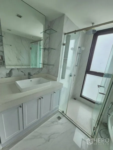 公寓 出租在Bang Rak, Bangkok - 带大镜子的洗手台，旁为透明玻璃淋浴间，整体大理石风格。