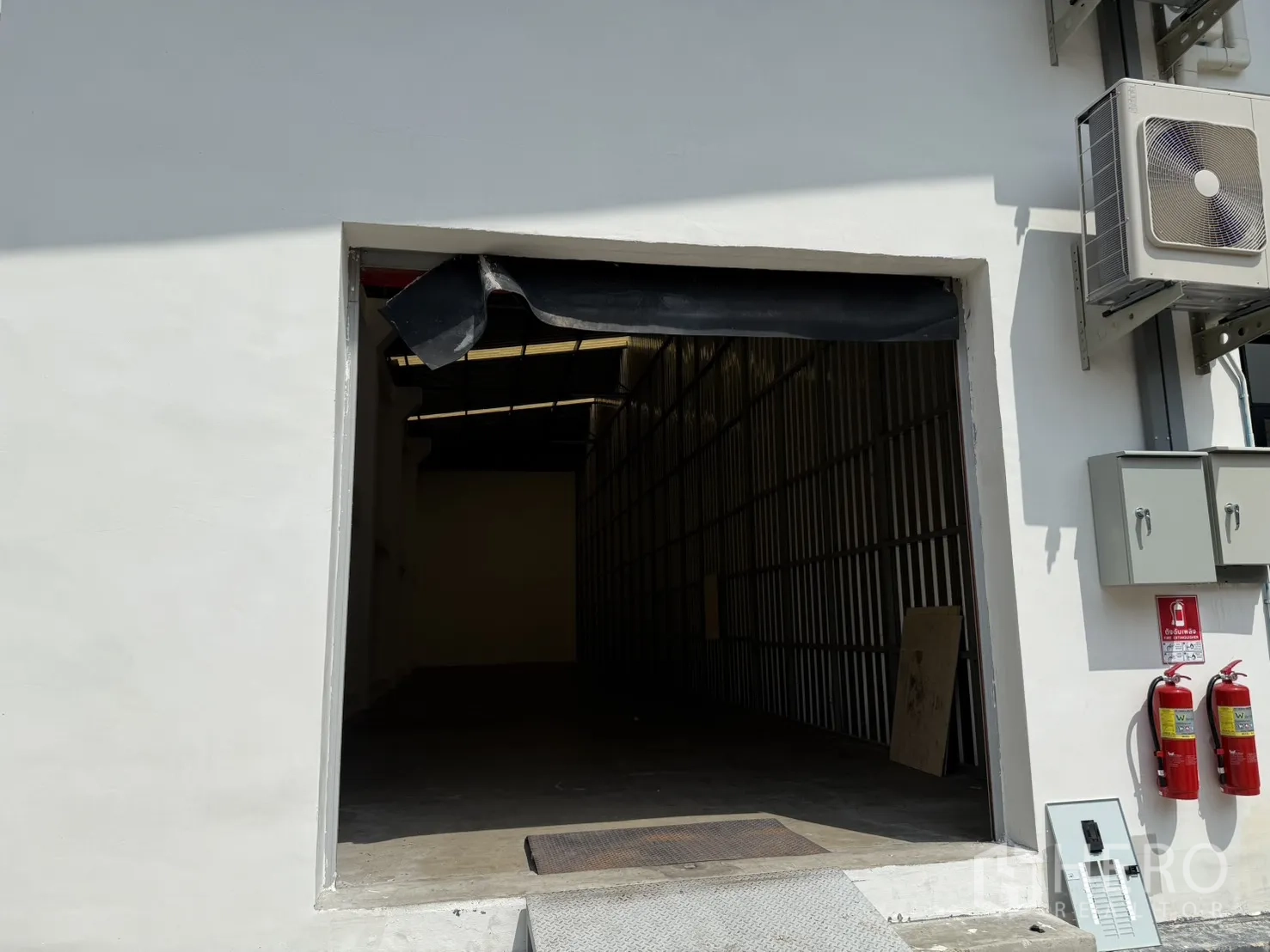 โกดัง for rent in Suan Luang, Bangkok - ประตูโกดังเปิดกว้างมีทางลาด พร้อมตู้ควบคุมไฟและถังดับเพลิงบนผนังด้านนอก