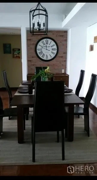 公寓 出租在Khlong Toei, Bangkok - 餐厅区设木质餐桌六椅、灯笼式吊灯与大号罗马数字挂钟，砖墙背景。