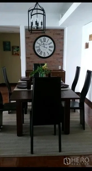 公寓 出租在Khlong Toei, Bangkok - 餐厅区设木质餐桌六椅、灯笼式吊灯与大号罗马数字挂钟，砖墙背景。