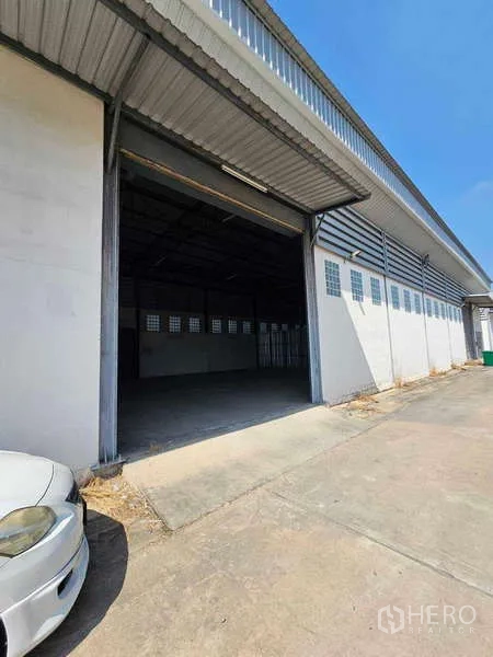 Warehouse for rent in Bang Bua Thong, Nonthaburi - Warehouse exterior with wide loading bay door, long eave cover and a concrete driveway.