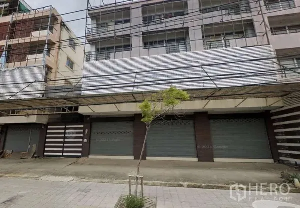 Shophouse for rent or sale in Bang Khun Thian, Bangkok - Street view of a multi-storey shophouse block with closed roller shutters and a wide canopy in Bang Khun Thian.
