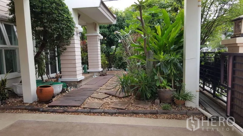 บ้าน ขายในMueang Nonthaburi, Nonthaburi - เฉลียงหน้าบ้านและสวนข้างบ้าน มีต้นไม้ใหญ่ กระถาง และทางเดินหินไปยังรั้ว