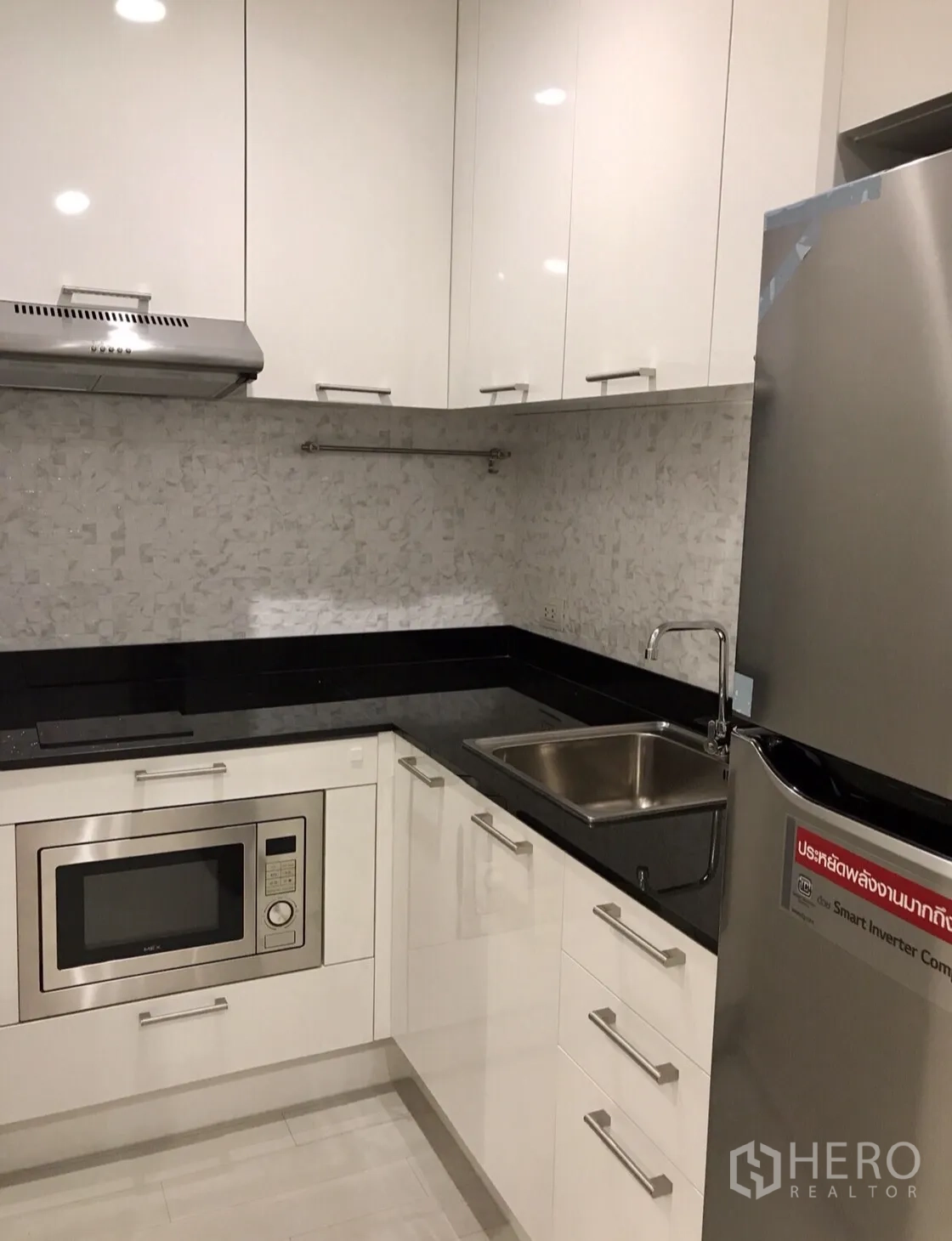 Condominium for rent in Pathum Wan, Bangkok - Sleek U-shaped kitchen with glossy white cabinets, black countertop, sink and built-in appliances.