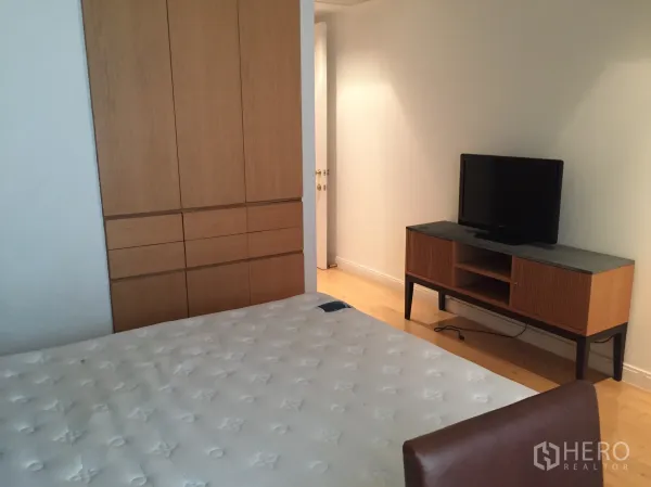 Condominium for rent or sale in Pathum Wan, Bangkok - Bedroom with built-in wardrobe, TV console and mattress on warm wood floors.