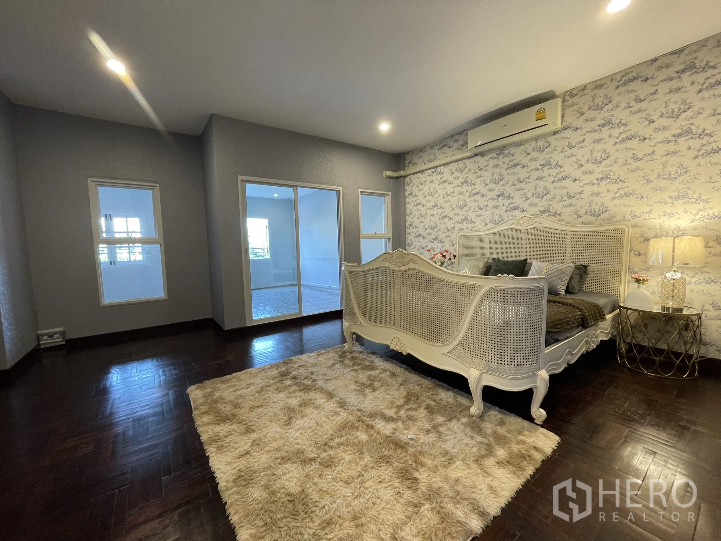 Shophouse for rent in Bang Kapi, Bangkok - Spacious bedroom with vintage cane bed, dark parquet floors and sliding glass to a bright enclosed room.