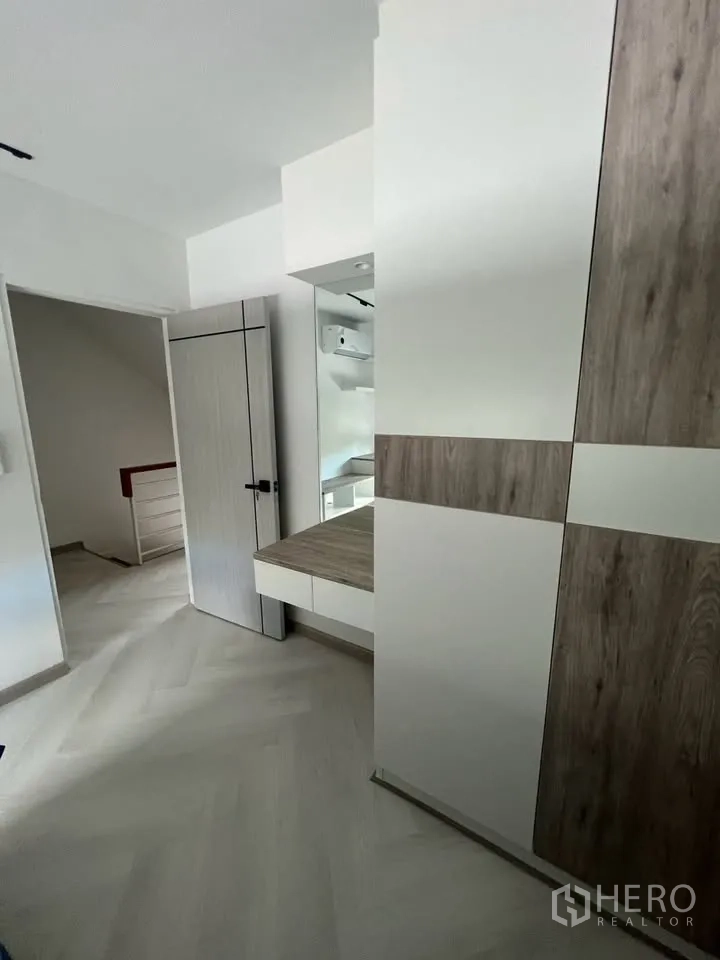 Townhouse for rent in Prawet, Bangkok - Bedroom corridor with built-in wardrobe, vanity and light herringbone floors.