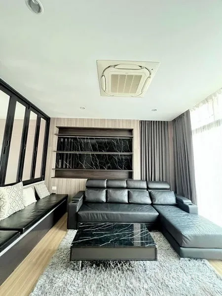 Townhouse for rent in Saphan Sung, Bangkok - Modern living room with black leather sectional, marble coffee table, built-in shelving and a large window.