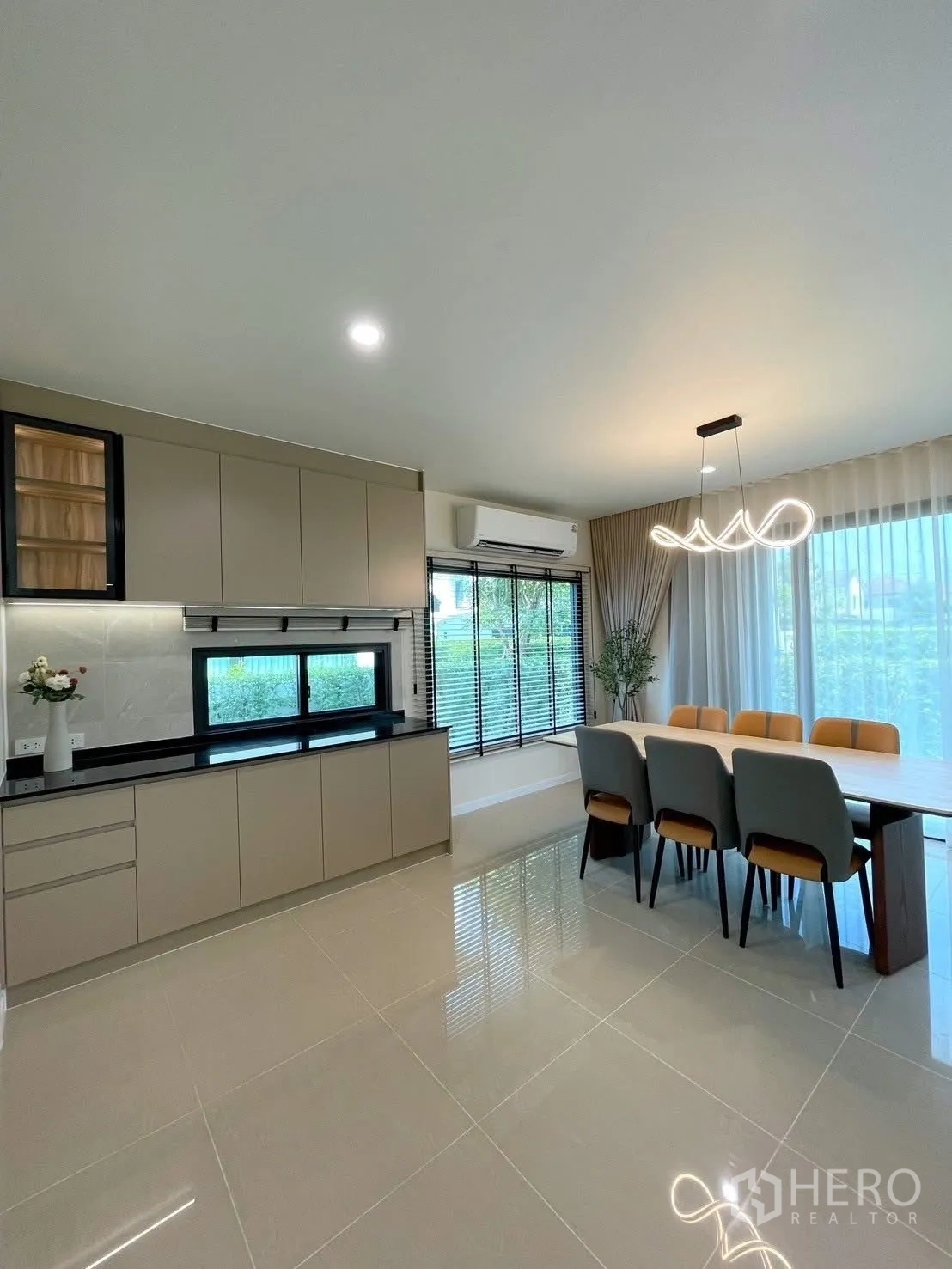 Detached House for rent in Bang Phli, Samut Prakan - Minimalist kitchen with beige cabinetry, black countertop and a six-seat dining table by windows.