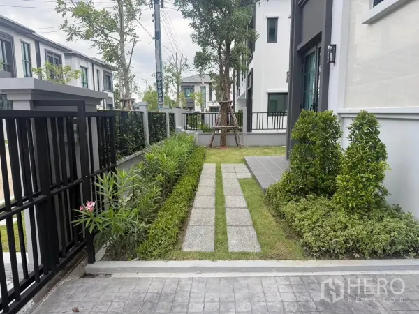 Detached House for rent in Bang Phli, Samut Prakan - Front garden with stepping-stone path, shrubs and a black metal gate by the driveway.
