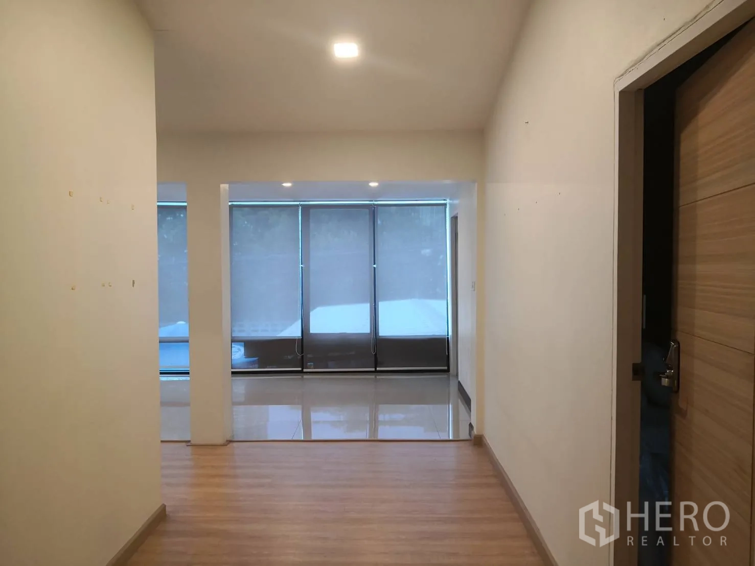 独栋房屋 for rent in Watthana, Bangkok - 入口走廊铺木地板，通向带大窗与卷帘的明亮起居区。