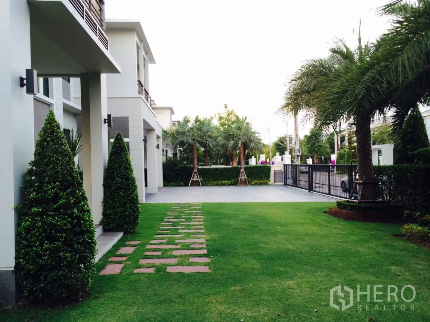 บ้าน ขายในLat Krabang, Bangkok - สวนหน้าบ้านมีทางเดินแผ่นปูเชื่อมไปยังประตูรั้วและลานจอดรถ