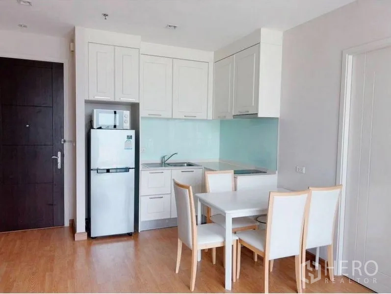 Condominium for rent in Watthana, Bangkok - Open kitchen and dining area with white cabinetry, fridge and four‑seat table.