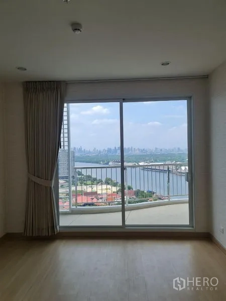 Condominium for sale in Yan Nawa, Bangkok - Bright room with sliding glass doors opening to a balcony and panoramic river and skyline view.