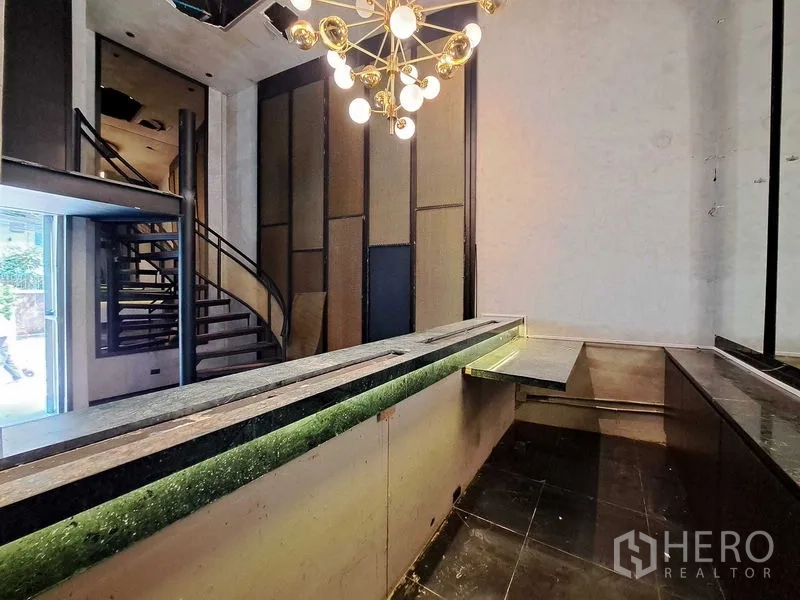 零售空间 出租在Watthana, Bangkok - 一层大理石吧台、现代吊灯与螺旋楼梯，挑高门厅气派十足。