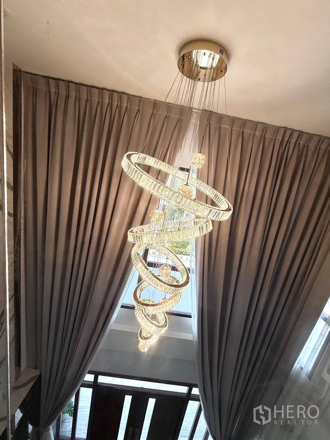 Detached House for rent in Wang Thonglang, Bangkok - Statement spiral chandelier hanging in a double-height foyer with tall curtains.