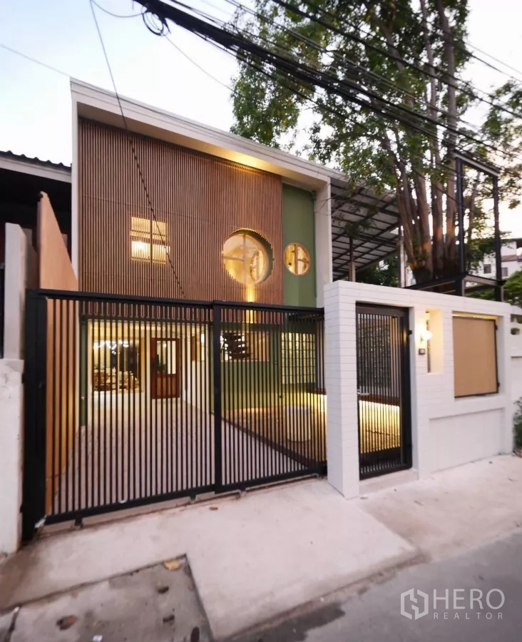 ทาวน์เฮาส์ ให้เช่าในWatthana, Bangkok - หน้าบ้านทาวน์เฮ้าส์สไตล์ญี่ปุ่นยามค่ำ มีหน้าต่างวงกลม ระแนงไม้ และประตูรั้วเหล็กสีดำแสงอบอุ่น