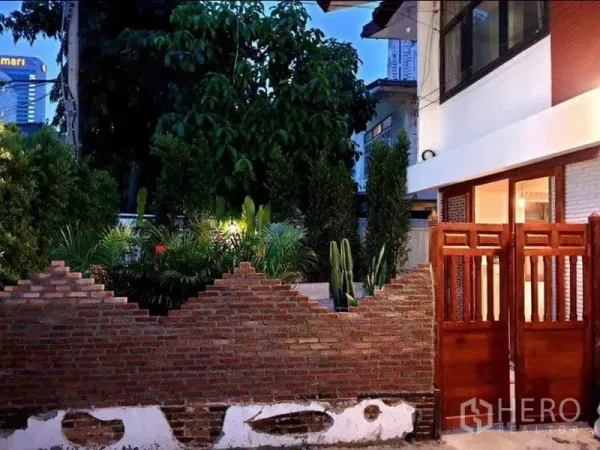 Detached House for rent in Pathum Wan, Bangkok - Evening exterior of detached house with brick fence, wooden gate and landscaped garden in Pathum Wan