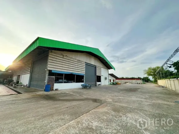 Warehouse for rent in Sai Noi, Nonthaburi - Exterior of the warehouse with expansive fenced yard suitable for truck turning and parking.