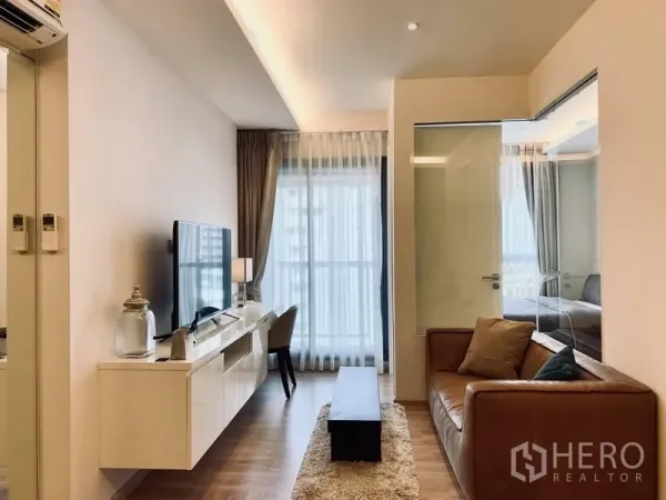 Condominium for rent in Watthana, Bangkok - Bright living room with leather sofa, TV console, and floor‑to‑ceiling window, with glass partition to the bedroom.