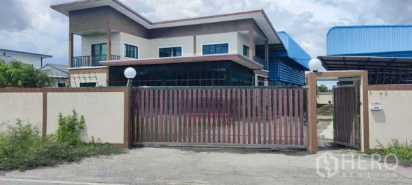 Warehouse for sale in Thung Khru, Bangkok - Gated entrance with two-storey office and blue-roof warehouse behind.