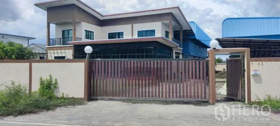 Warehouse for sale in Thung Khru, Bangkok - Gated entrance with two-storey office and blue-roof warehouse behind.