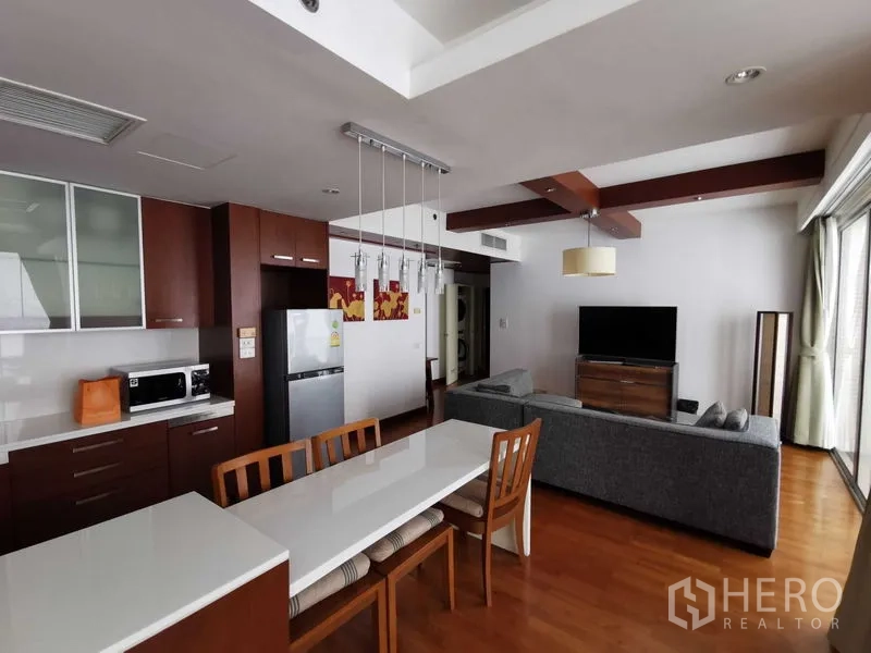 Condominium for rent in Pathum Wan, Bangkok - Kitchen and living room overview with breakfast bar, sofa seating, and TV.