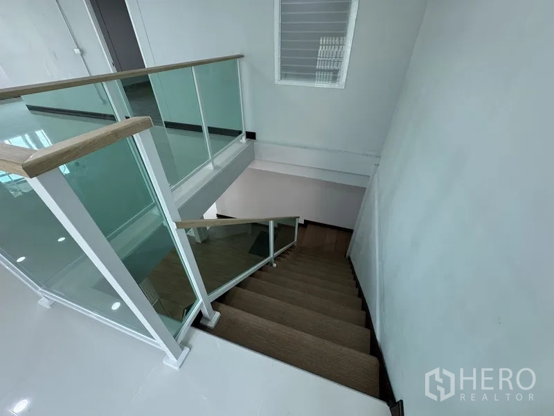 Townhouse for sale in Bueng Kum, Bangkok - Staircase with wood steps and glass railing connecting two floors.