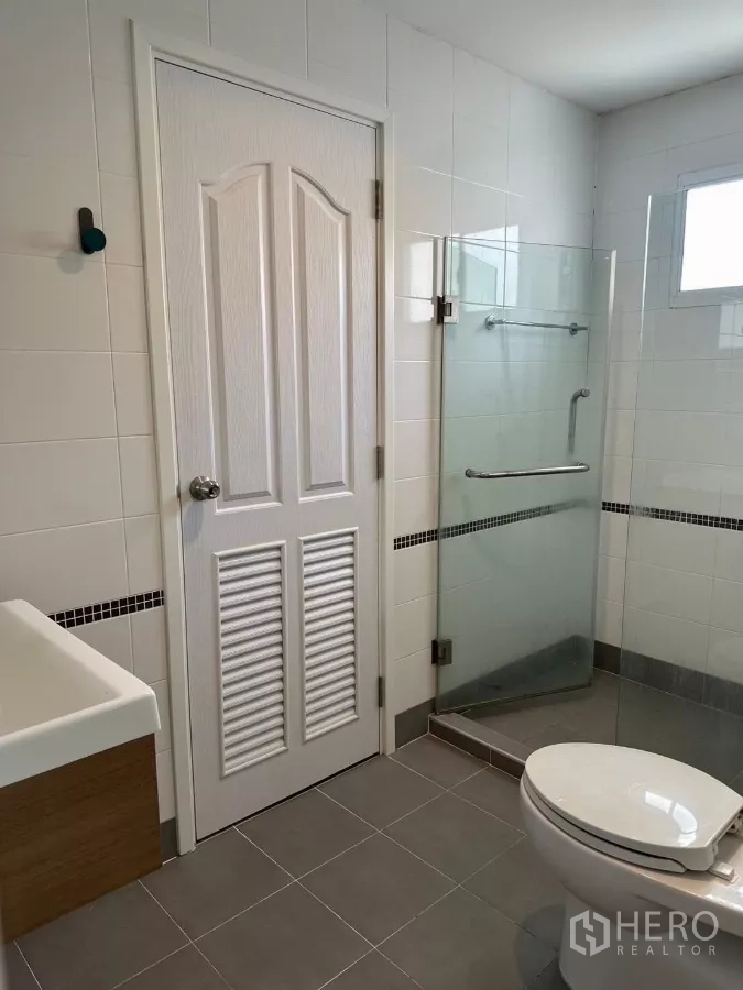 บ้าน ให้เช่าในSuan Luang, Bangkok - ห้องน้ำอีกห้องมีฉากกั้นกระจก อ่างล้างหน้า และประตูบานลูกฟักสีขาว.