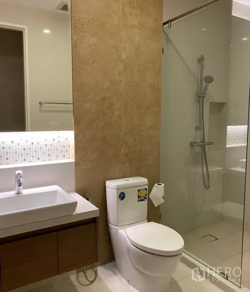 Condominium for rent in Khlong Toei, Bangkok - Second bathroom with vanity, toilet and glass-enclosed rain shower.