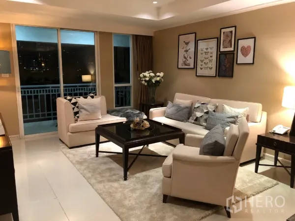 คอนโด ให้เช่าในWatthana, Bangkok - มุมนั่งเล่นโซฟาโทนอ่อน มีภาพตกแต่ง โต๊ะกลาง และประตูออกสู่ระเบียงเห็นสกายไลน์ยามค่ำ