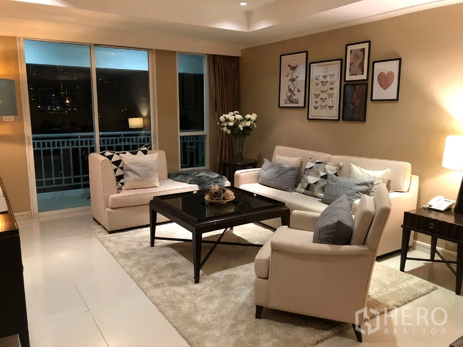 คอนโด ให้เช่าในWatthana, Bangkok - มุมนั่งเล่นโซฟาโทนอ่อน มีภาพตกแต่ง โต๊ะกลาง และประตูออกสู่ระเบียงเห็นสกายไลน์ยามค่ำ
