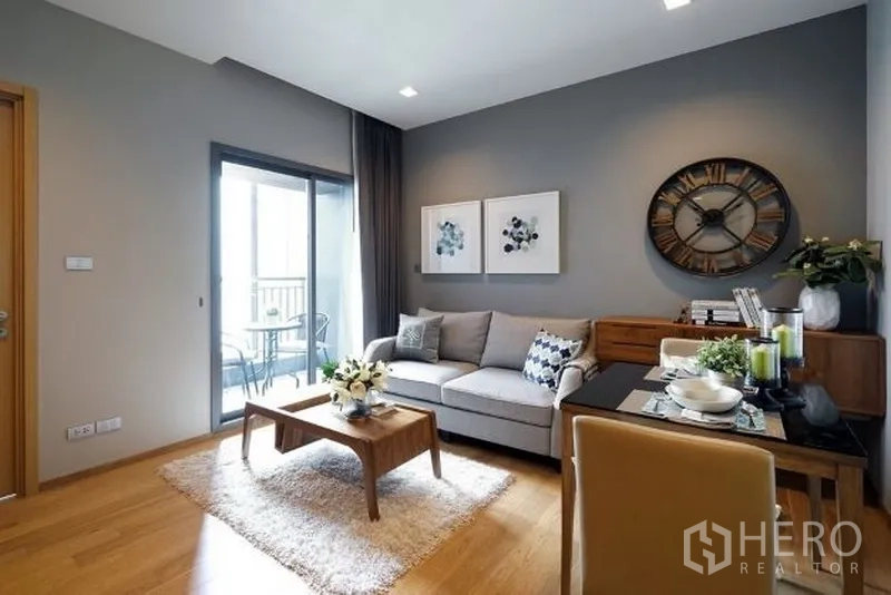 คอนโด ให้เช่าในWatthana, Bangkok - ห้องนั่งเล่นสว่าง ผนังเทา โซฟา มุมทานอาหาร และประตูสไลด์ออกสู่ระเบียงคอนโดสมัยใหม่ในกรุงเทพฯ