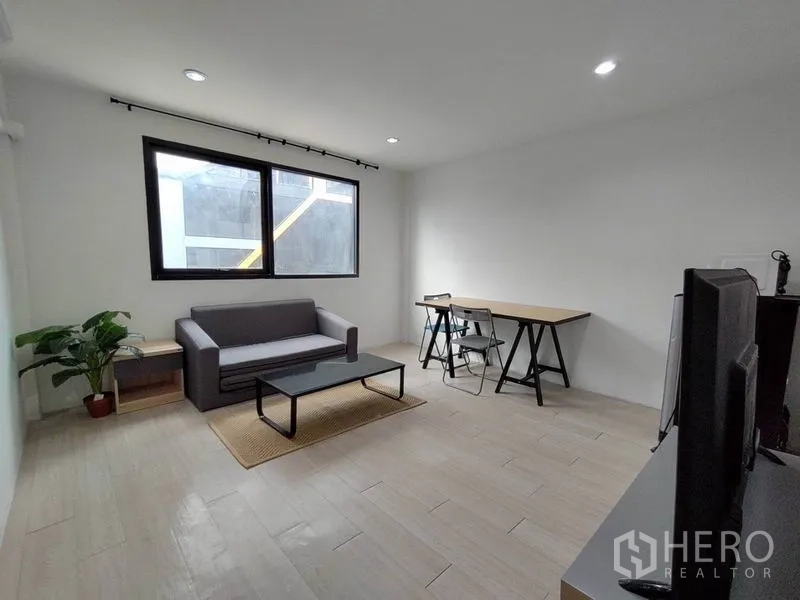 带办公室的家 出租 - 极简客厅/办公区，沙发、落地窗、书桌与椅子。