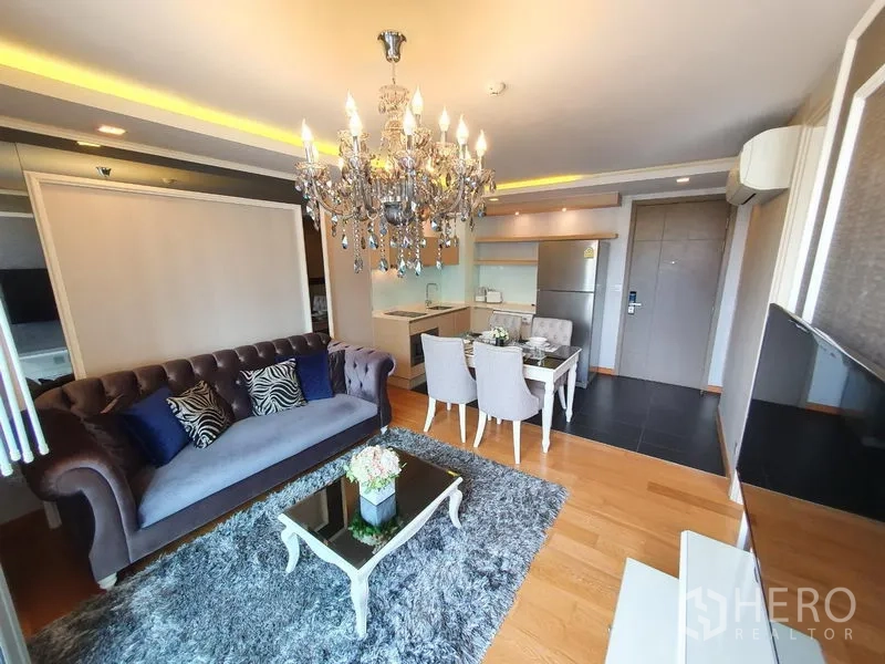 公寓 出租在Watthana, Bangkok - 客厅角度：天鹅绒沙发、玻璃茶几与吊灯相连开放式厨房。