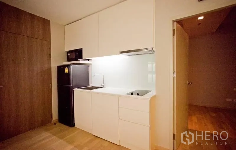 Condominium for rent or sale in Watthana, Bangkok - Compact white kitchenette with cooktop, sink, microwave and refrigerator.
