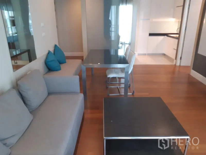 公寓 出租或出售在Khlong Toei, Bangkok - 开放式起居区，灰色沙发与黑色餐桌，通向白色厨房的木地板