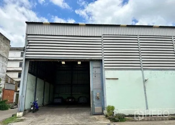 คลังสินค้า ขายในBang Bon, Bangkok - ด้านหน้าโกดังโลหะ ประตูม้วนขนาดใหญ่เปิดอยู่ ในย่านบางบอน กรุงเทพฯ