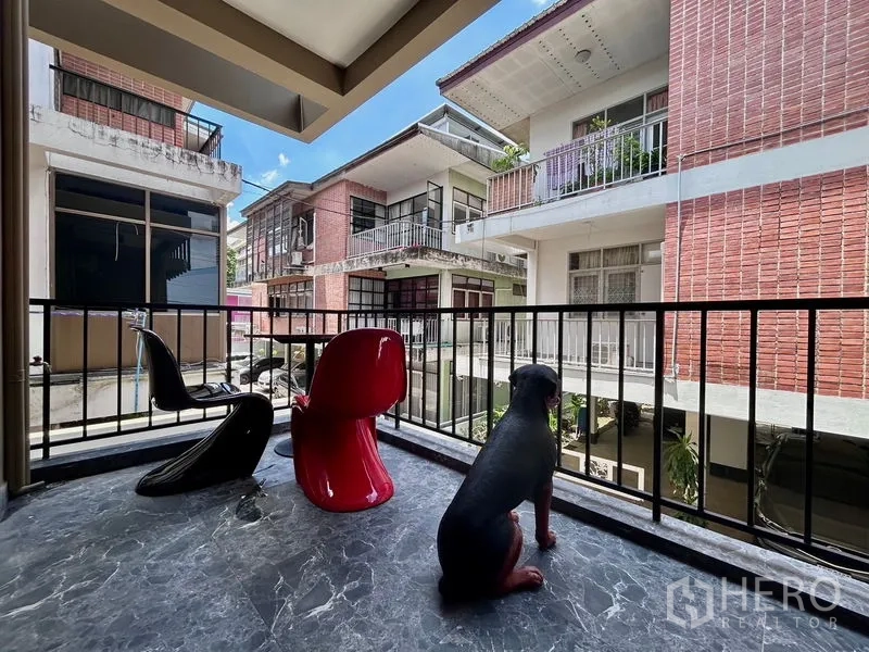 Apartment for rent in Khlong Toei, Bangkok - Covered balcony with stone-look flooring and designer chairs overlooking surrounding low-rise brick buildings.