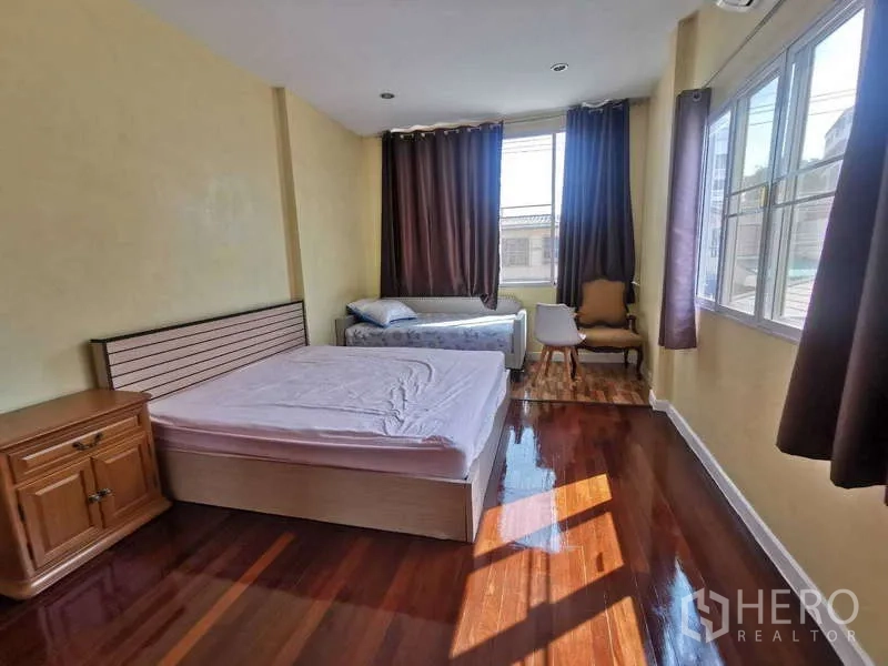 ทาวน์เฮาส์ ให้เช่าในChatuchak, Bangkok - ห้องนอนสว่าง พื้นไม้ เตียงคู่ โต๊ะข้าง และหน้าต่างบานใหญ่พร้อมผ้าม่าน.