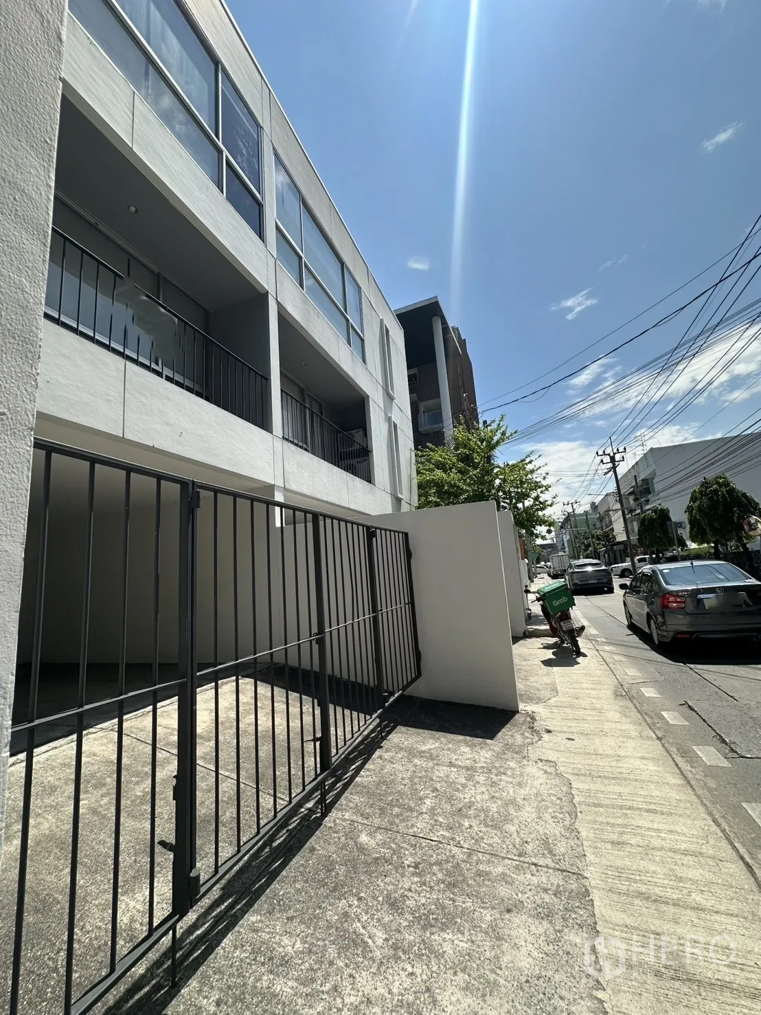 Home Office for rent in Phra Khanong, Bangkok - Street-side perspective of the building and sliding gate on a sunny day.