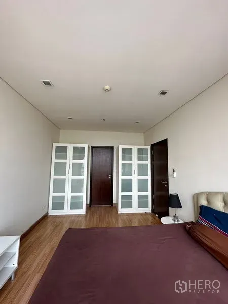 Condominium for sale in Watthana, Bangkok - Bedroom with wood floors and two glass-front wardrobes beside dark wooden doors.